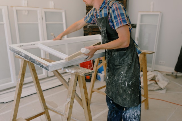 person in a apron painting a window frame white